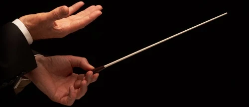 A conductor hand holding a baton against a dark background