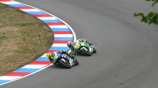 Two motorcycle racers leaning into a corner beside a red, white, and blue track kerb.