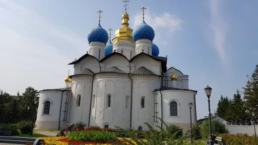 Blue and gold domes above the white Annunciation Cathedral in the Kazan Kremlin, with flowers in the foreground.