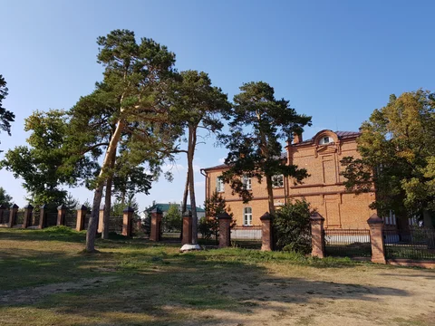 Tall trees shade a red-brick building and a grassy courtyard.
