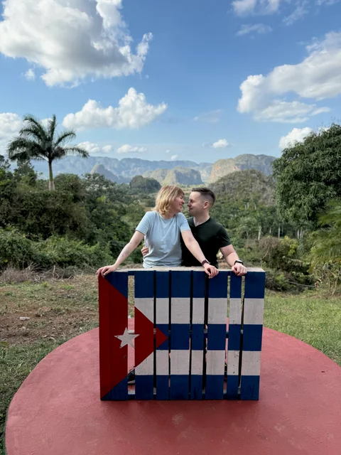 Lena and me behind a wooden Cuban flag, with the valley and hills behind us