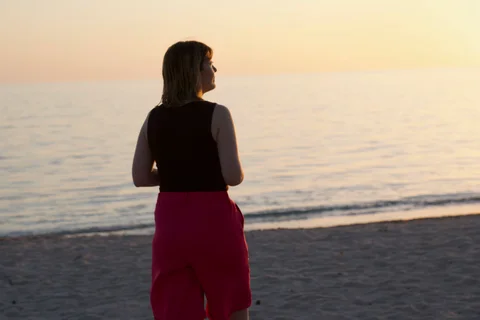 Lena looking out over the sea at sunset, with warm light on her hair