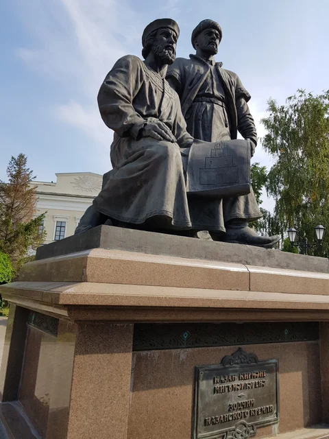 A bronze monument to two builders, one seated and one standing, holding drawings.