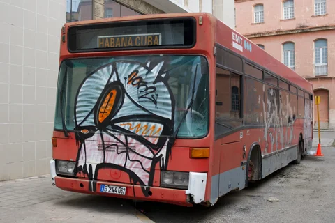 A red bus with a painted face across its windscreen and a Habana Cuba destination sign