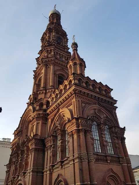 An ornate red-brick bell tower rises into a blue sky.