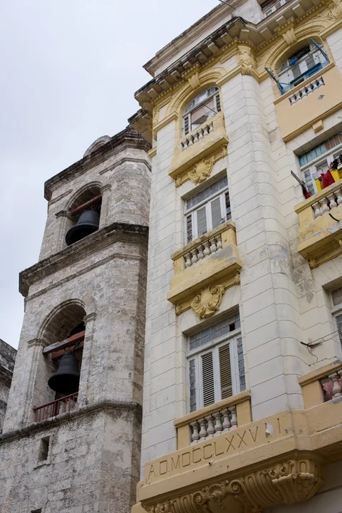 A stone bell tower beside a yellow facade with shuttered windows and small balconies