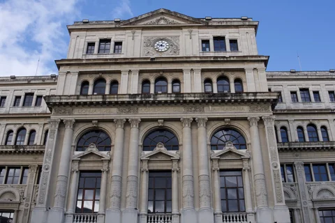 A stone facade with tall columns, arched windows and a clock beneath the pediment