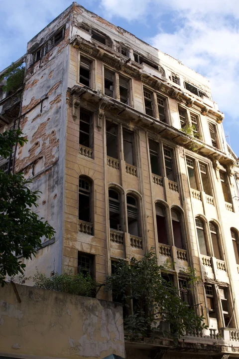 A tall Havana building with peeling plaster and plants growing from its balconies