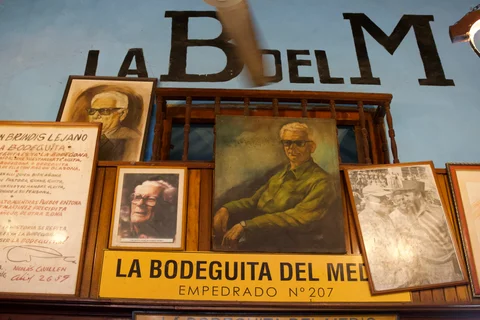 Framed portraits and writing above a La Bodeguita del Medio sign on a blue wall