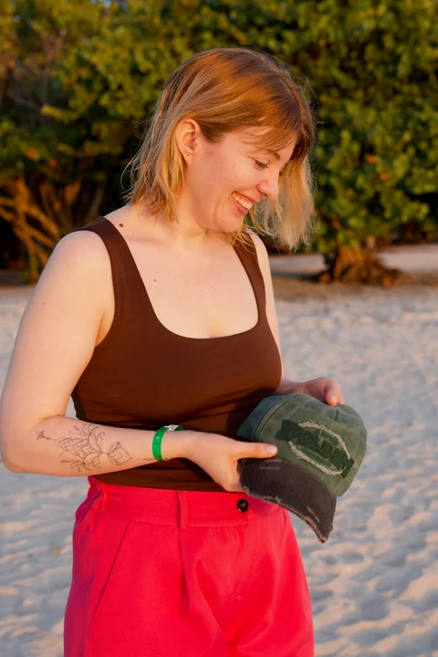 Lena smiling in the golden evening light, holding her green cap on the beach