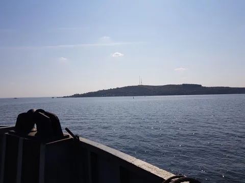 Open water and a distant wooded bank, seen over the dark edge of the ferry.