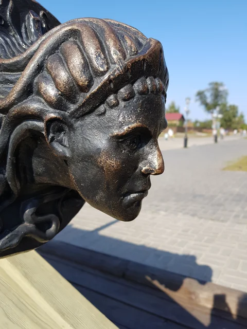 Close-up of a bronze face in profile beside a sunlit path.