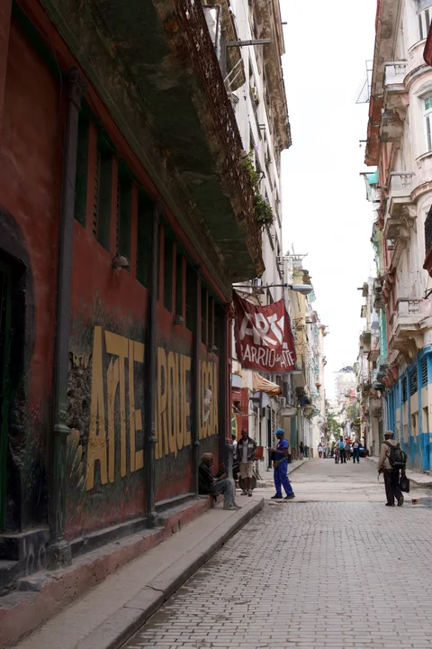 A narrow Havana street with a red art banner and large lettering on a workshop wall