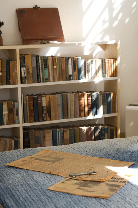 Sunlight on bookshelves, with old newspapers and a large metal key on a blue bedspread