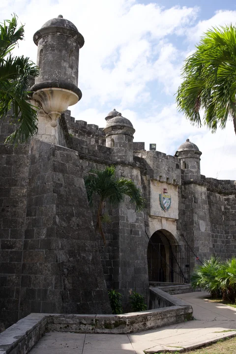 A stone fortress gateway with turrets, a coat of arms and palm trees