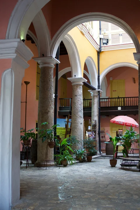 White arches and stone columns in the Havana Club courtyard, with potted plants and a red parasol