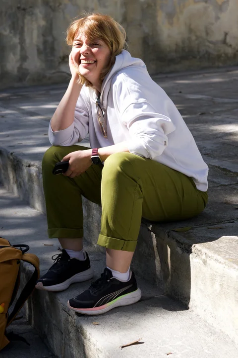 Lena in a white hoodie and green trousers smiling while sitting on stone steps