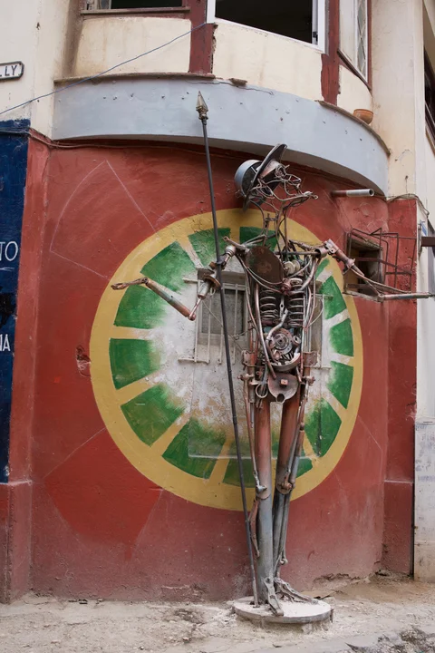 A tall metal figure with a spear outside a red-painted workshop