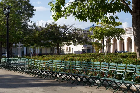 Rows of green metal chairs beside a flowering hedge in Parque José Martí, Cienfuegos