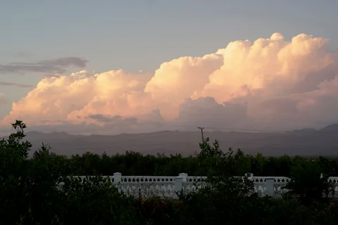 Golden evening clouds above dark hills and trees, with a white balustrade in the foreground