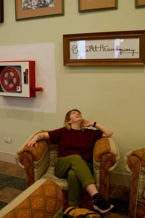 Lena looking up at a framed Hemingway signature from an armchair at Hotel Ambos Mundos