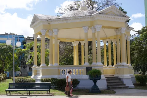 The yellow and white bandstand in Parque Vidal, Santa Clara, with benches and people walking past