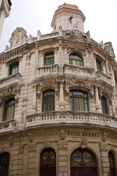 An ornate corner building with curved balconies, carved stonework and a small tower