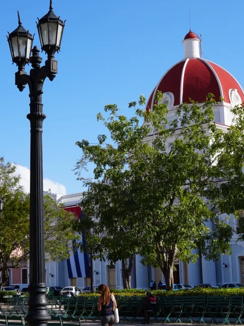 The red dome of the Palacio de Gobierno behind trees and a double streetlamp in Parque José Martí, Cienfuegos