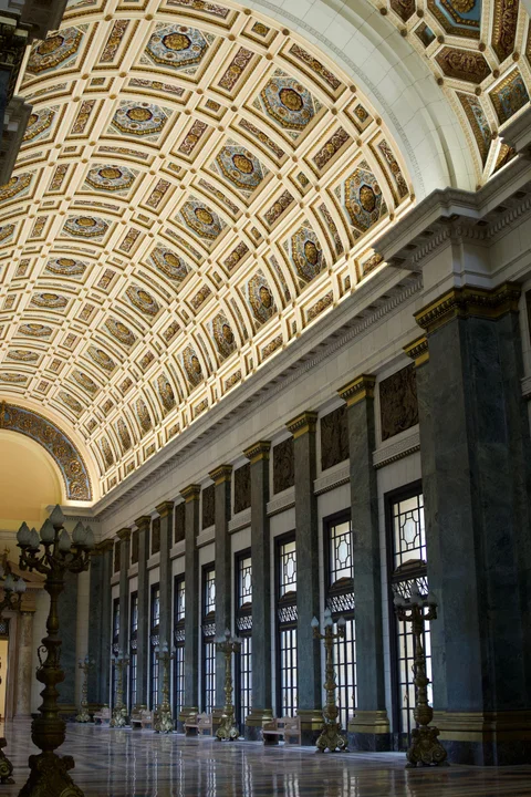 The Capitol’s richly decorated vaulted ceiling above a long row of windows and green stone columns