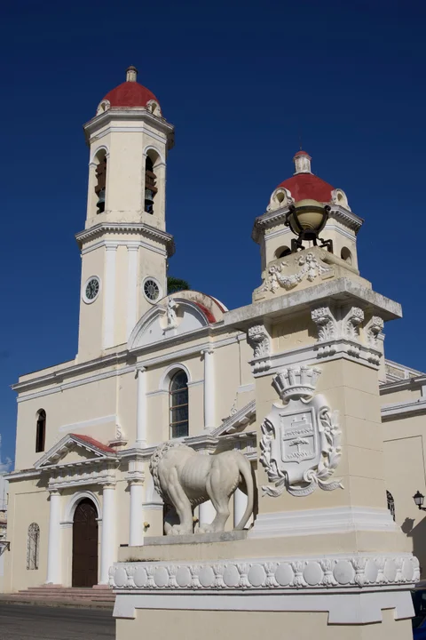 The yellow and white Catedral de la Purísima Concepción in Cienfuegos, with a stone lion in the foreground