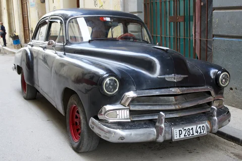 A black vintage car with red wheels and a chrome bumper parked on a narrow Havana street