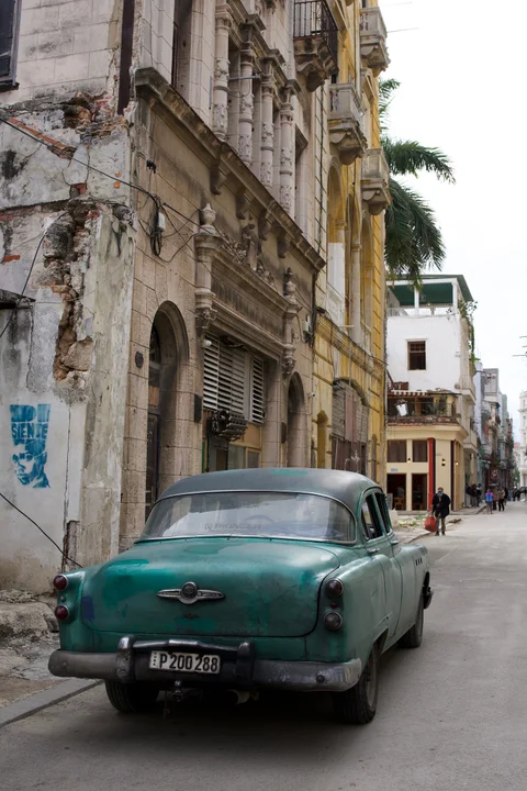 A turquoise vintage car parked beside weathered facades in Havana