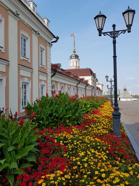 Red and yellow flowers line a path beside a pale building and black street lamps.