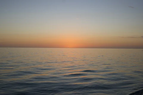 Soft orange light above the sea after sunset, with small waves in the foreground