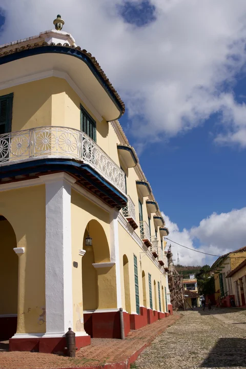 The curved white balcony and yellow arches of Palacio Brunet above a cobbled street in Trinidad