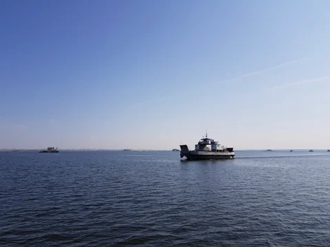 A passing ferry crosses open water beneath a pale blue sky.