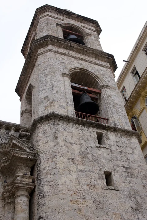 Two bells in a weathered stone tower, photographed from the street below