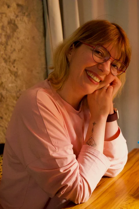 Lena smiling at a table in César Jazz Club, wearing glasses and resting her cheek against her hands