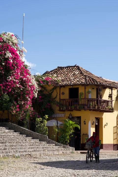 The yellow Los Conspiradores restaurant beside stone steps in Trinidad, with a wooden balcony and flowering bougainvillea
