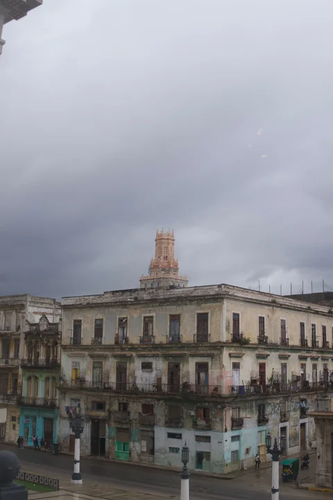 Weathered buildings across the street from the Capitol, with a tower rising behind them under grey clouds