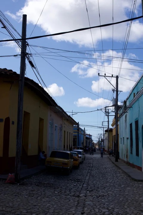 A cobbled street in Trinidad lined with colourful houses, parked cars and overhead wires