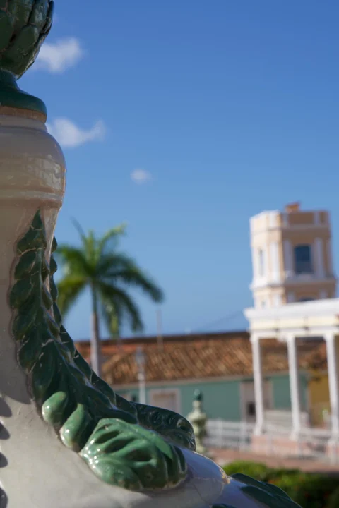 A green and cream ceramic ornament in Plaza Mayor, with a palm and tower softly out of focus behind it