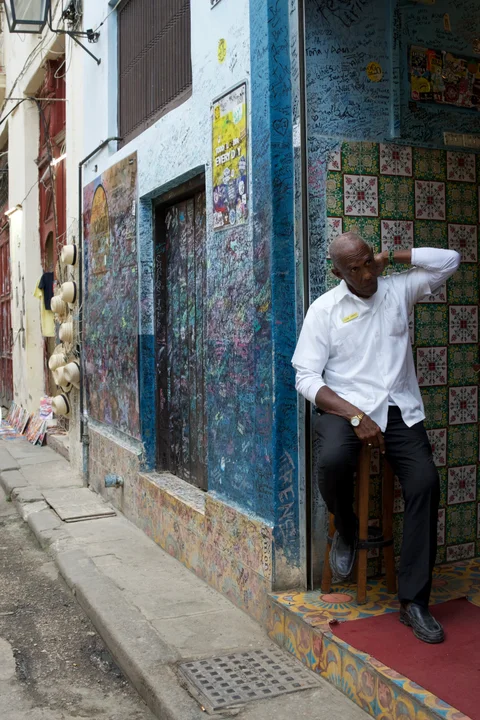 A man in a white shirt sitting in a blue doorway covered with writing and decorative tiles