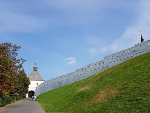 A path follows the white Kremlin wall towards a gateway, beside a green slope.