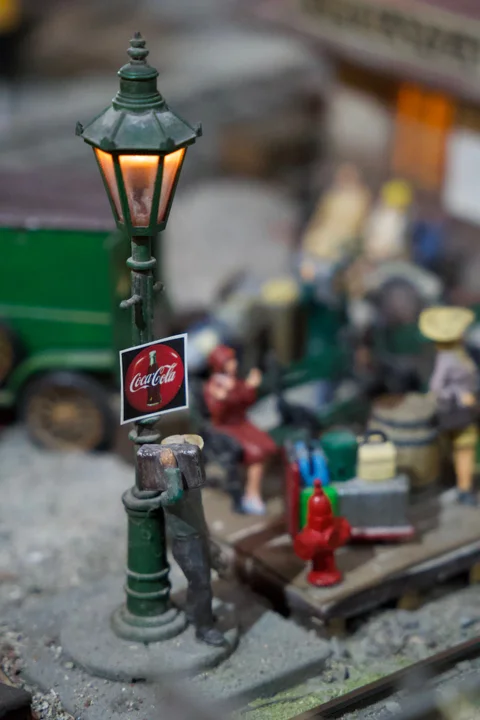 A tiny lit street lamp with a Coca-Cola sign among figures and vehicles in the Havana Club diorama