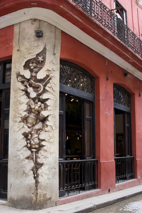 A relief of musical instruments and small figures on a red Havana facade
