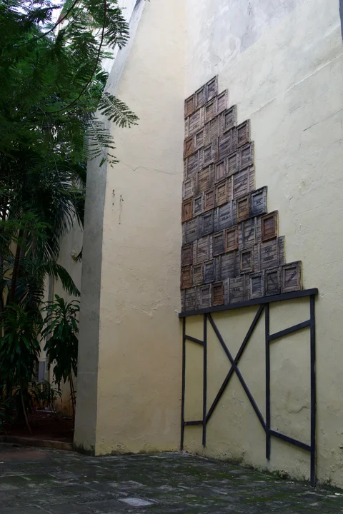 Wooden crate panels stacked into a wall artwork beside tropical plants in a Havana courtyard