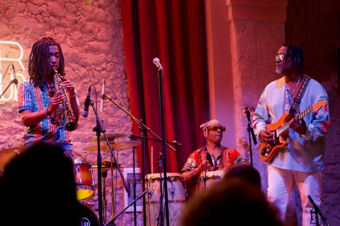 A saxophonist, percussionist and guitarist playing on the jazz club stage in front of the audience