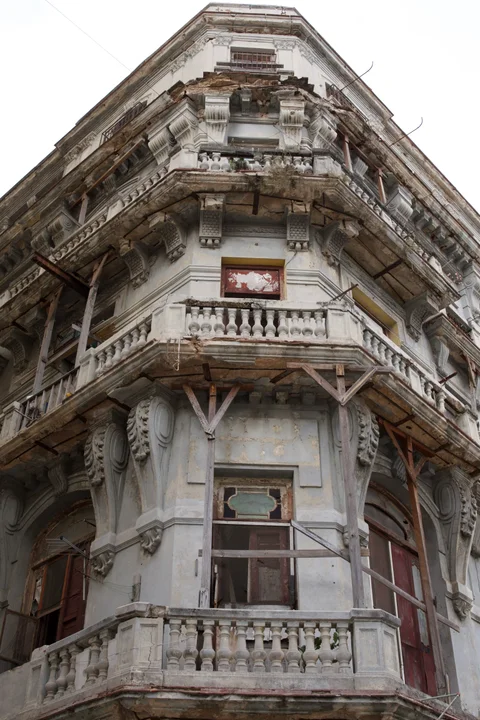 Weathered corner balconies with carved brackets and wooden supports on an old Havana building