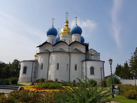 The white Annunciation Cathedral with blue and gold domes and flowers in the foreground.